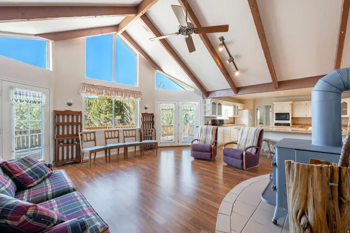 Living area with high vaulted ceiling, dark wood finished floors, ceiling fan, and beam ceiling