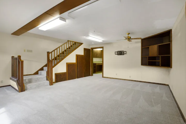 Finished basement featuring light colored carpet, a ceiling fan, and stairs