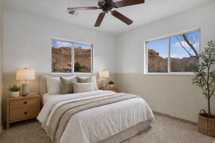 Carpeted bedroom with a ceiling fan and multiple windows