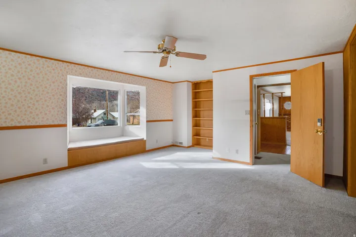 Spare room featuring wallpapered walls, crown molding, built in shelves, ceiling fan, and carpet floors