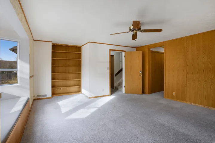 Unfurnished bedroom featuring light carpet, ensuite bath, crown molding, and a ceiling fan