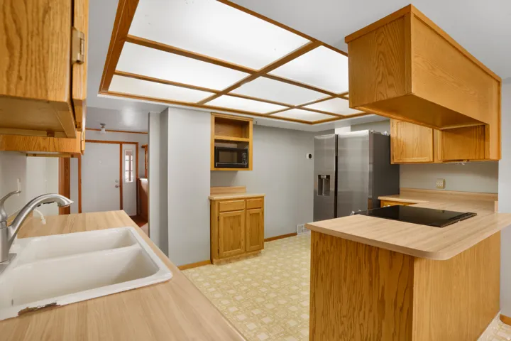 Kitchen featuring light countertops, brown cabinetry, black appliances, open shelves, and a peninsula