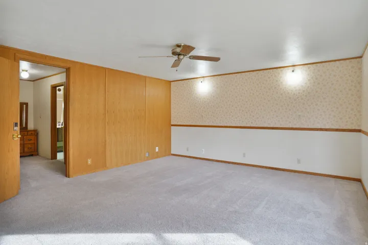 Empty room with ornamental molding, light carpet, wallpapered walls, and ceiling fan