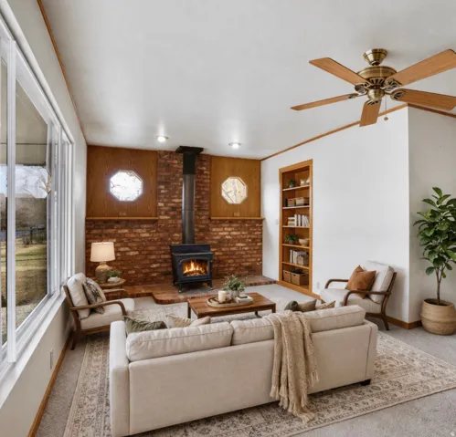 Living area with carpet floors, a wood stove, built in features, ceiling fan, and ornamental molding
