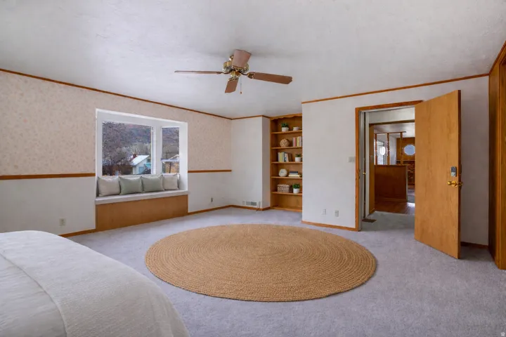 Bedroom featuring wallpapered walls, multiple windows, ornamental molding, light colored carpet, and a textured ceiling