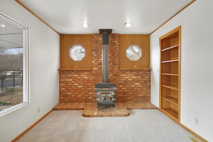 Unfurnished living room with a wood stove, carpet flooring, and ornamental molding