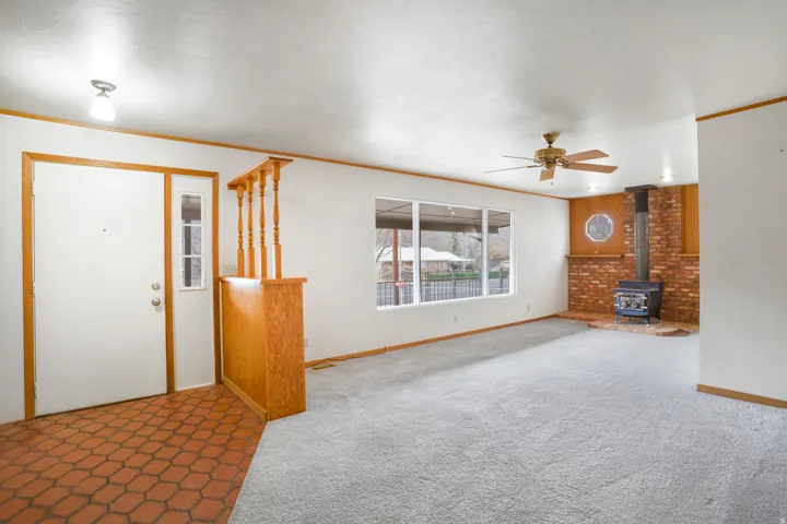 Unfurnished living room with a wood stove, ornamental molding, carpet flooring, and a ceiling fan