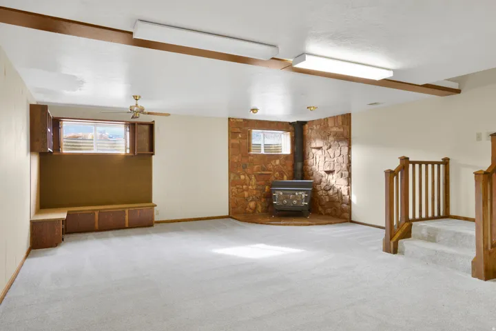 Below grade area featuring a wood stove, carpet floors, stairway, and ceiling fan