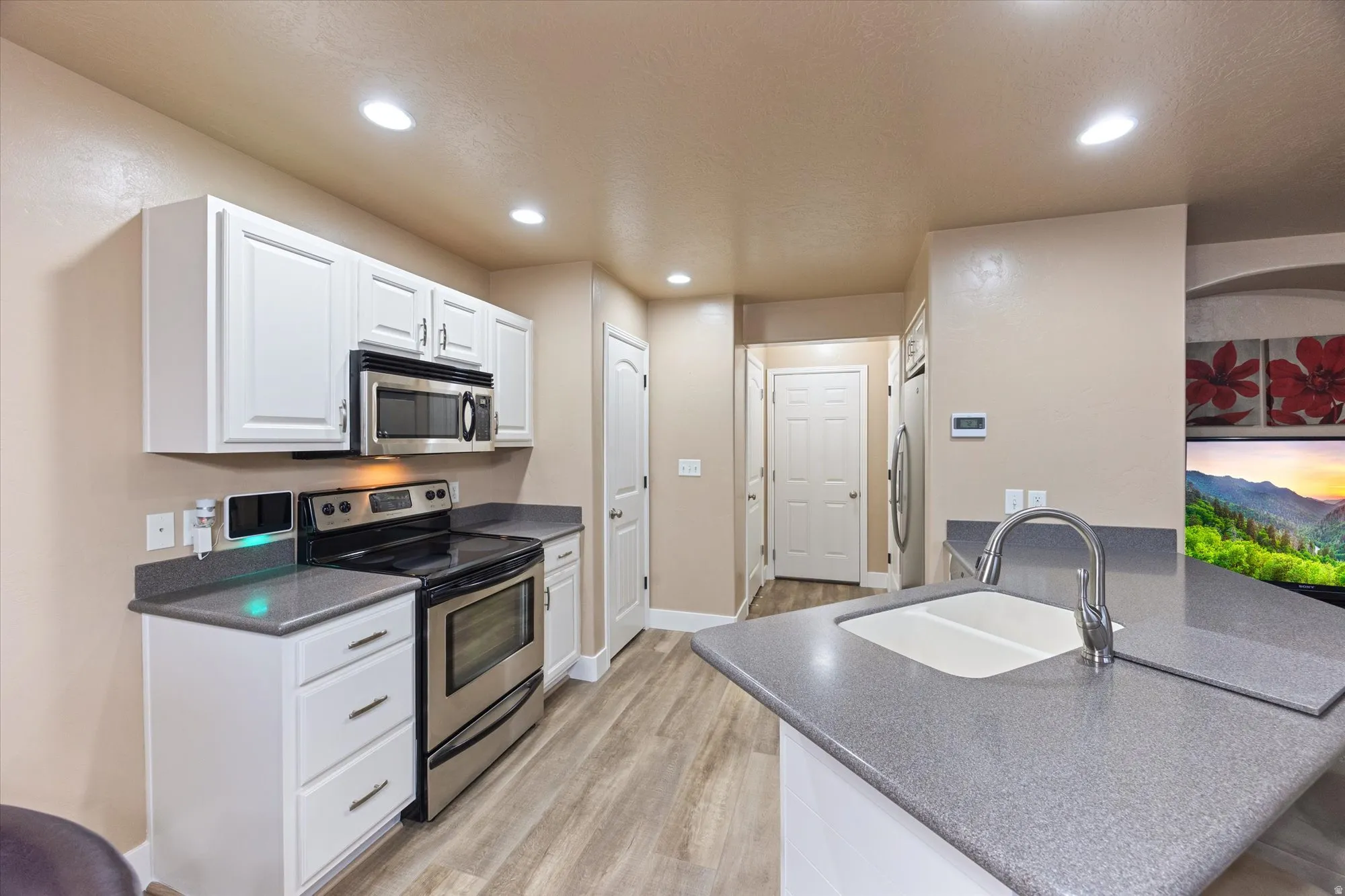 Kitchen with stainless steel appliances, white cabinetry, light wood-style flooring, dark stone counters, and recessed lighting