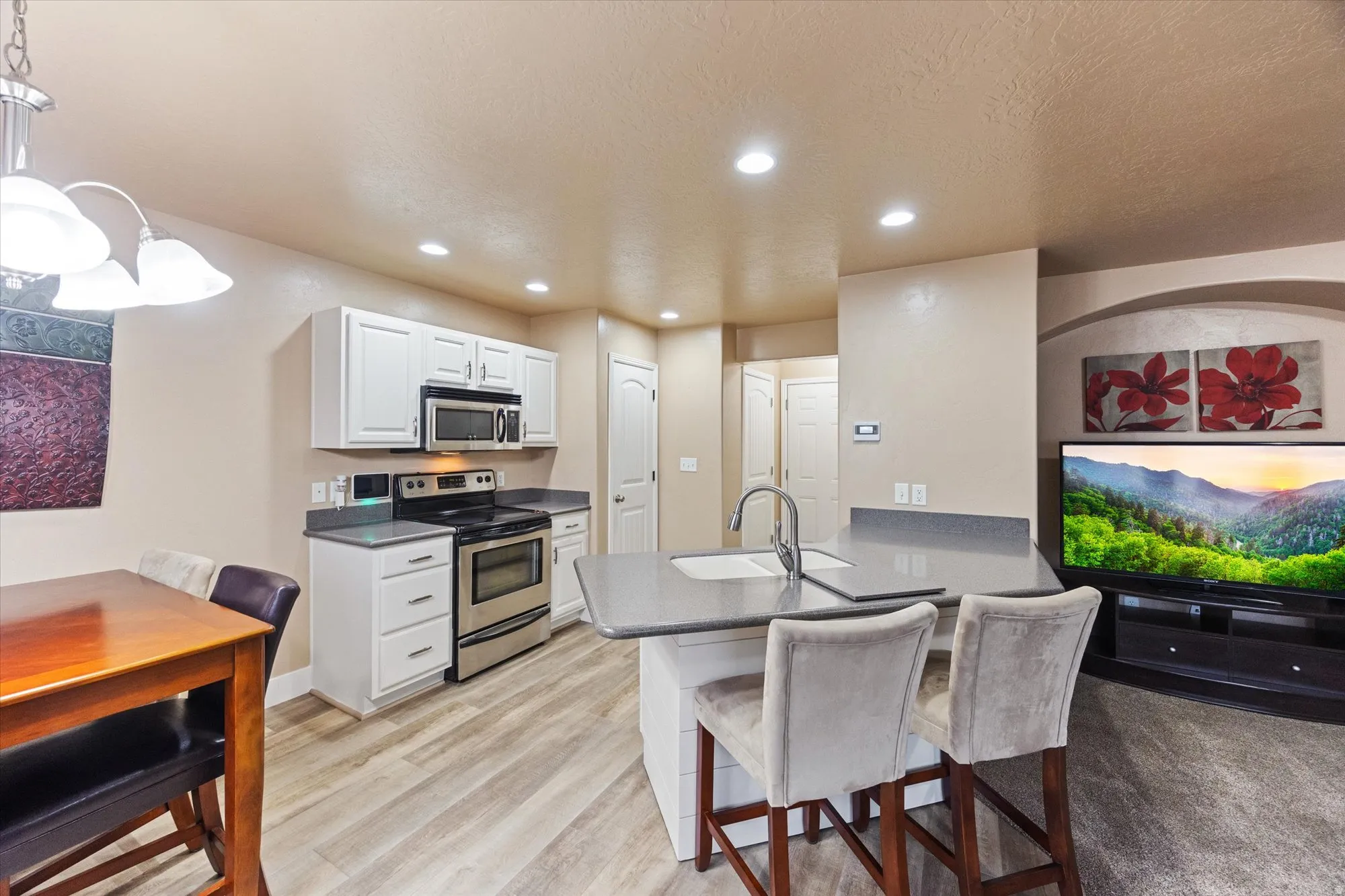 Kitchen featuring stainless steel appliances, a kitchen bar, white cabinetry, hanging light fixtures, and a peninsula