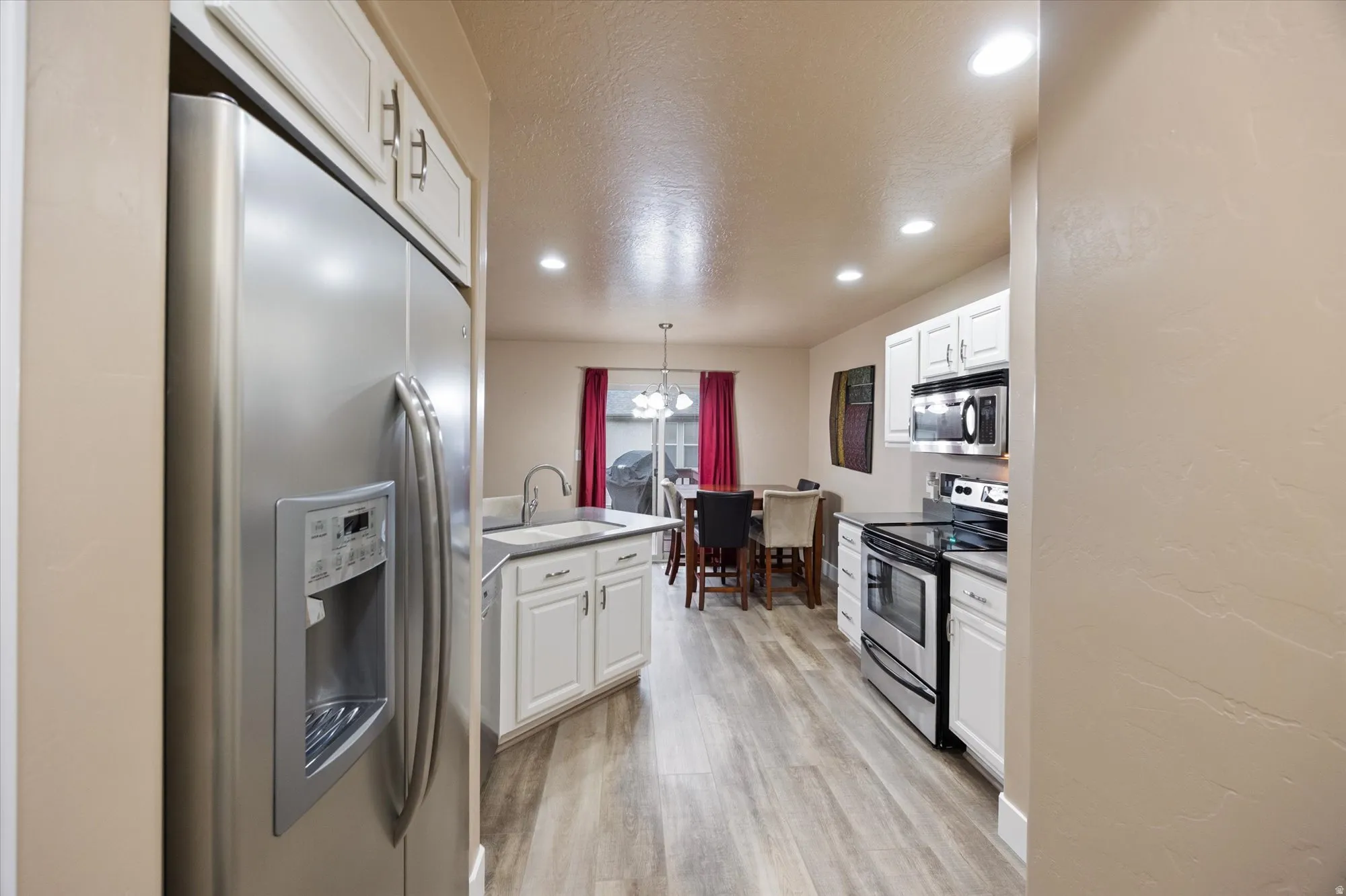 Kitchen featuring stainless steel appliances, white cabinetry, a chandelier, recessed lighting, and light wood-type flooring