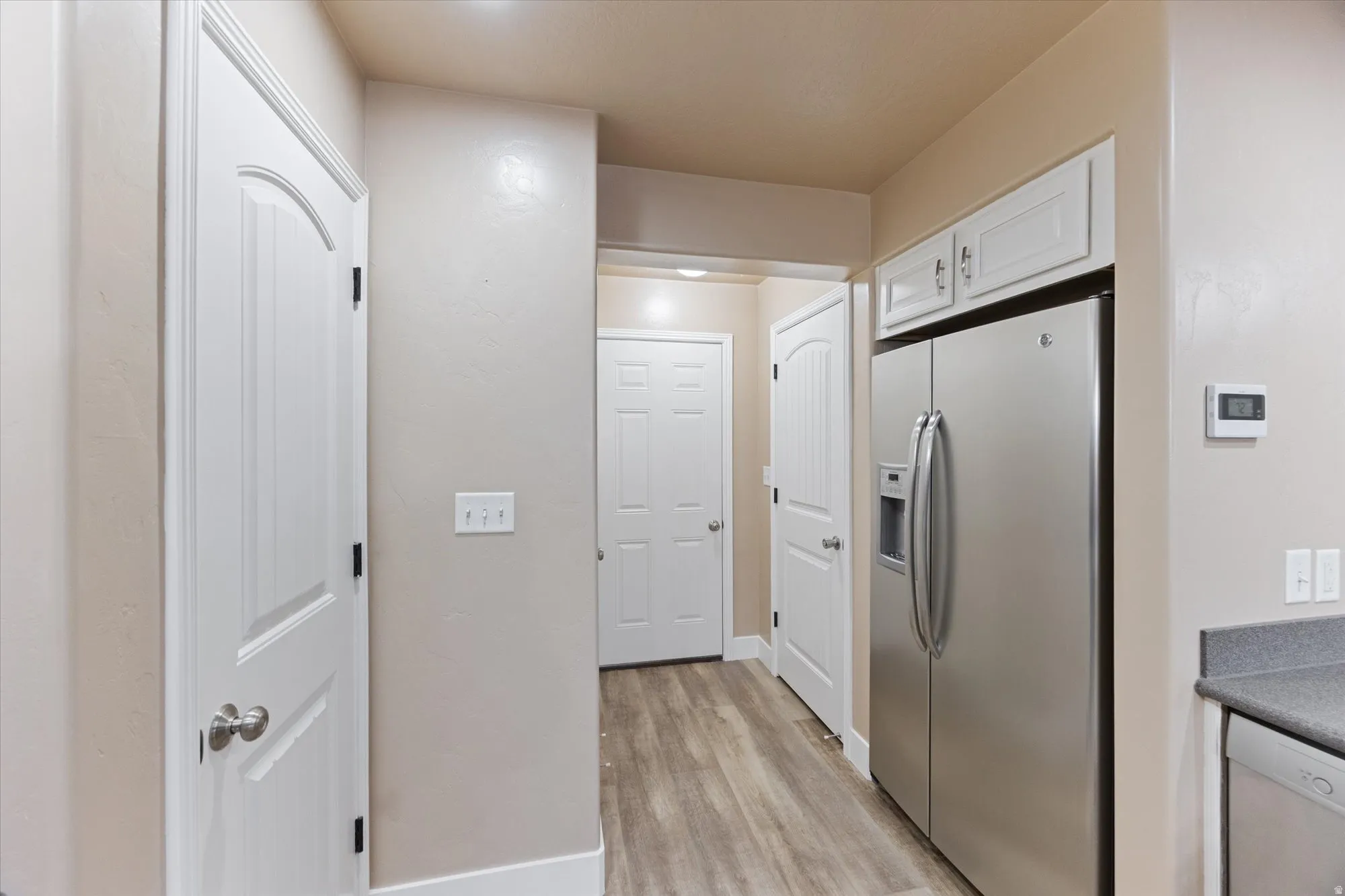 Kitchen featuring stainless steel refrigerator with ice dispenser, dishwasher, white cabinets, light wood-type flooring, and dark countertops