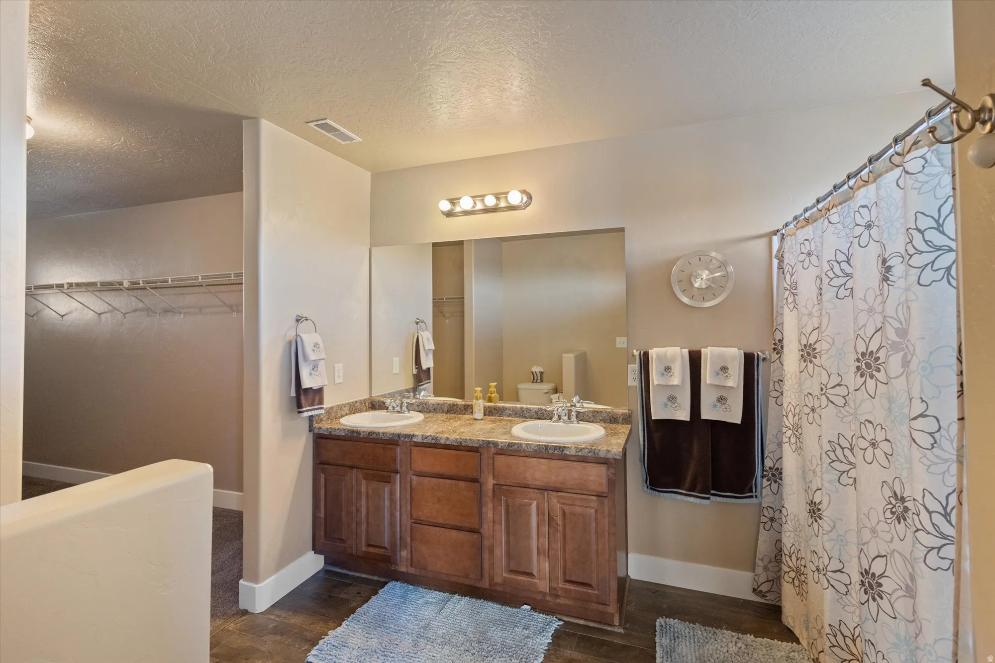 Full bath featuring a textured ceiling, double vanity, a spacious closet, a shower with shower curtain, and dark wood-style flooring
