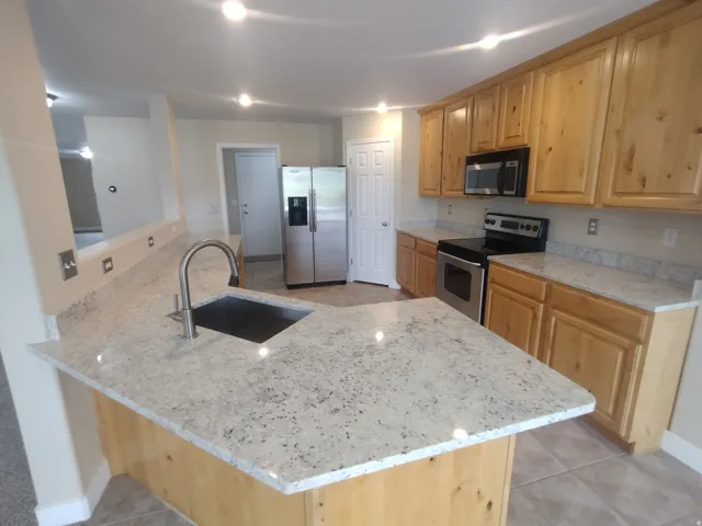 Kitchen featuring a peninsula, appliances with stainless steel finishes, light stone counters, and light tile patterned floors