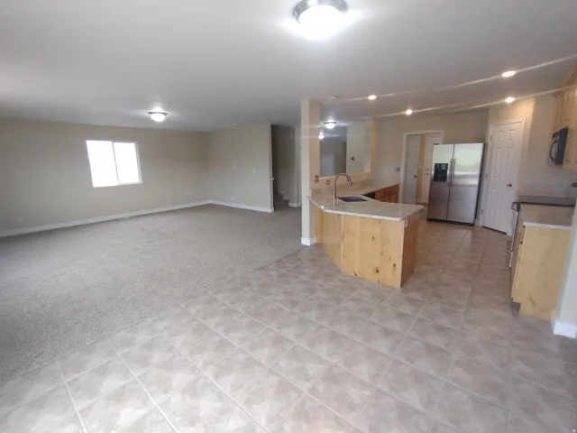 Kitchen featuring a peninsula, light colored carpet, stainless steel fridge, light countertops, and open floor plan