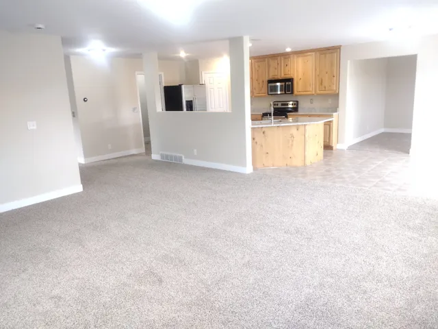 Kitchen featuring light colored carpet, appliances with stainless steel finishes, open floor plan, light brown cabinetry, and recessed lighting