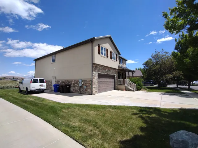 View of property exterior featuring stone siding, driveway, stucco siding, an attached garage, and a yard