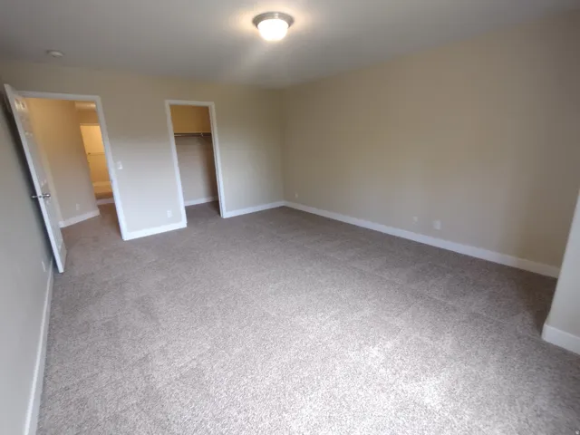 Unfurnished bedroom with a walk in closet and light carpet