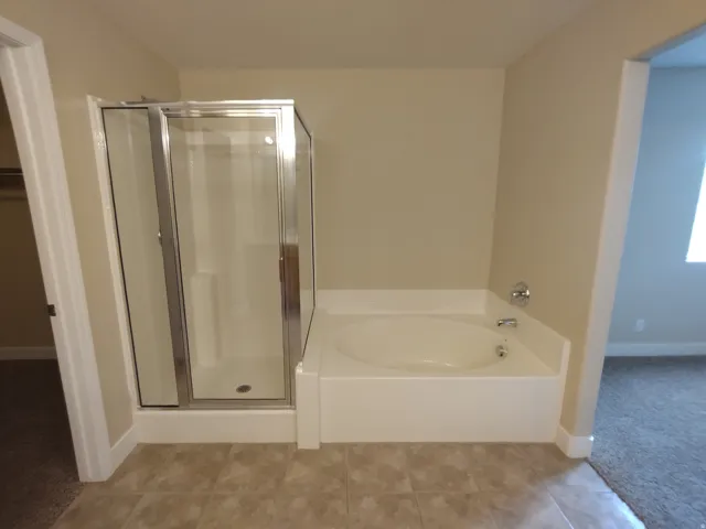 main bath Full bath featuring a stall shower, a garden tub, a walk in closet, tile patterned floors, and carpet