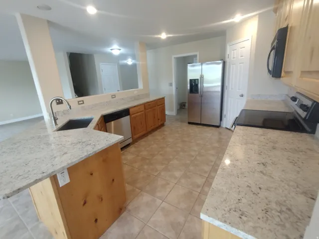 Kitchen featuring a peninsula, stainless steel appliances, light stone counters, and light tile patterned floors