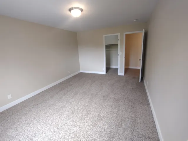 Unfurnished bedroom featuring a walk in closet and light carpet