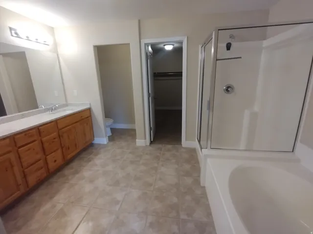Main Bedroom Bath with a spacious closet, vanity, a stall shower, a garden tub, and light tile patterned floors