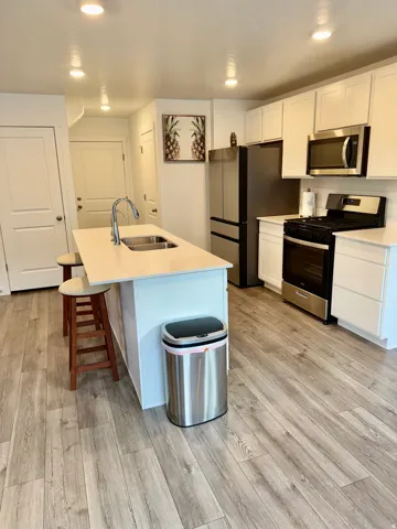 Kitchen featuring appliances with stainless steel finishes, white cabinets, recessed lighting, a center island with sink, and a kitchen breakfast bar. Quartz