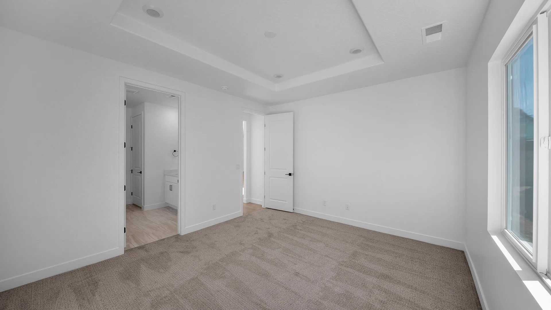 Unfurnished bedroom with light carpet, ensuite bath, and a raised ceiling