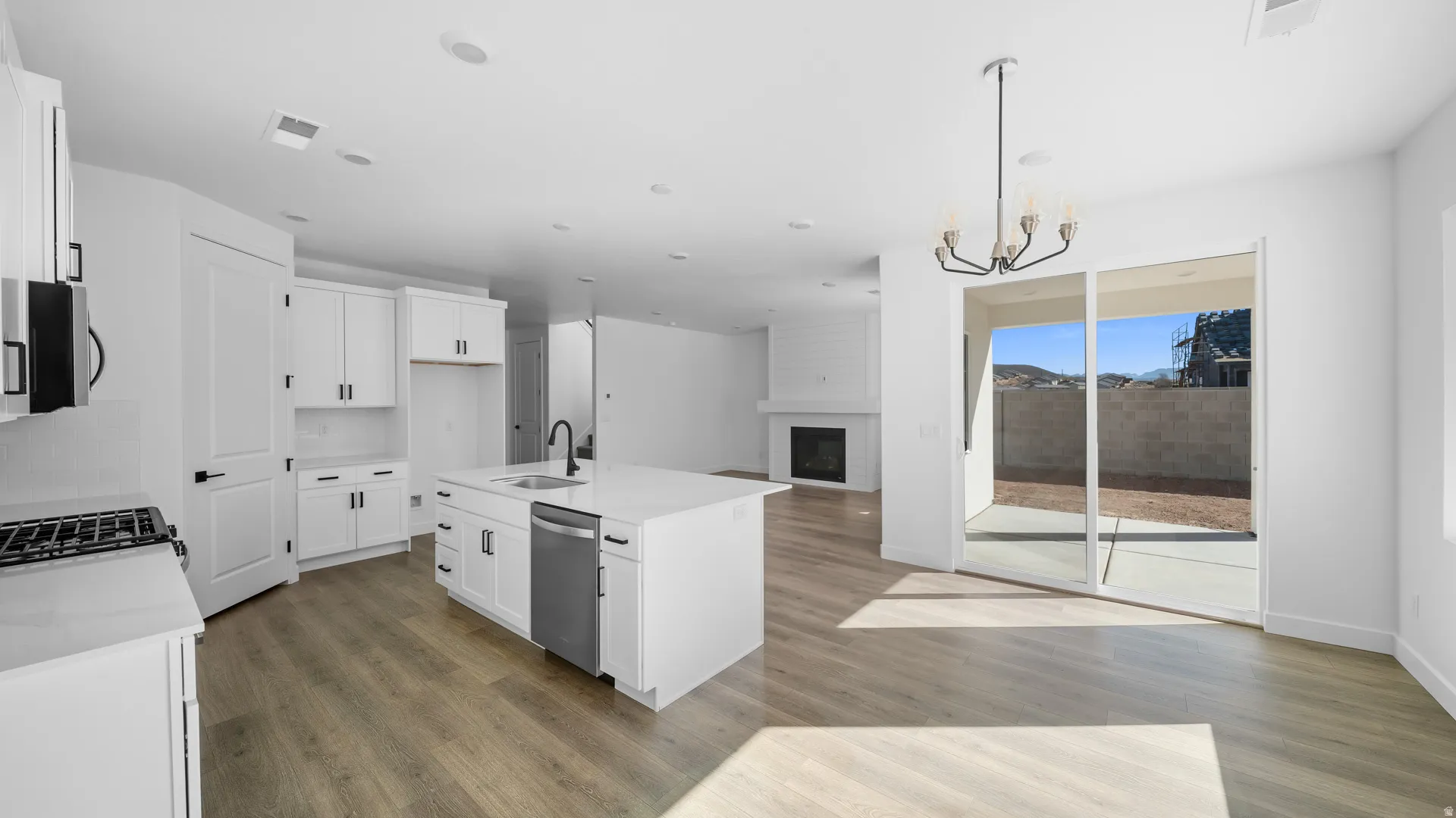 Kitchen featuring a large fireplace, an island with sink, white cabinetry, open floor plan, and light stone countertops