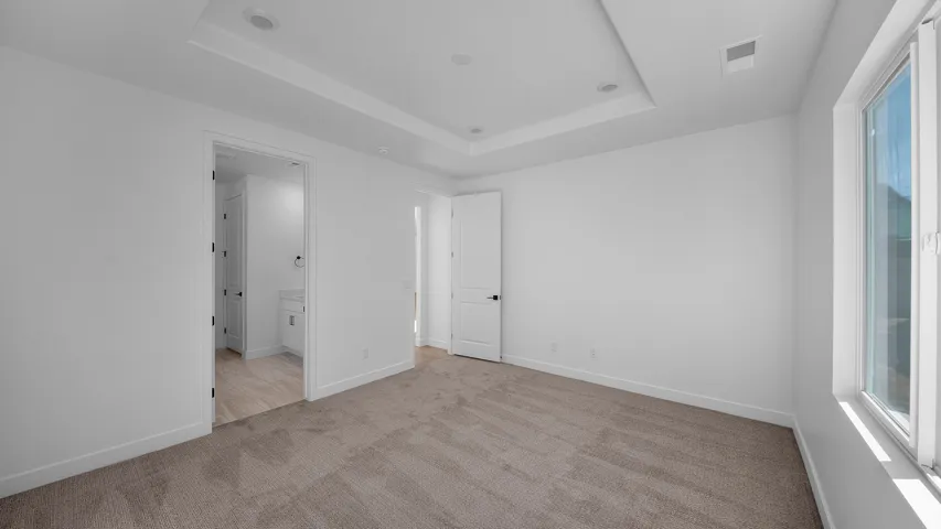 Unfurnished bedroom with light carpet, ensuite bath, and a raised ceiling