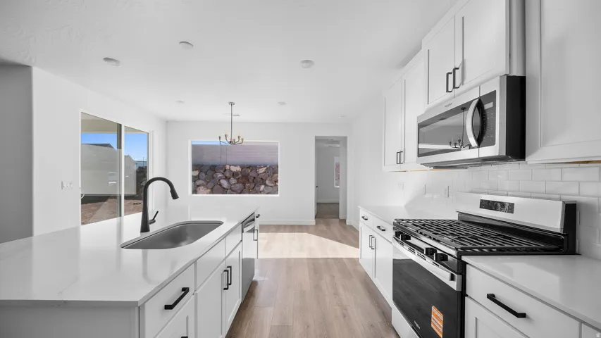 Kitchen with stainless steel appliances, light wood-style floors, a center island with sink, white cabinetry, and hanging lights