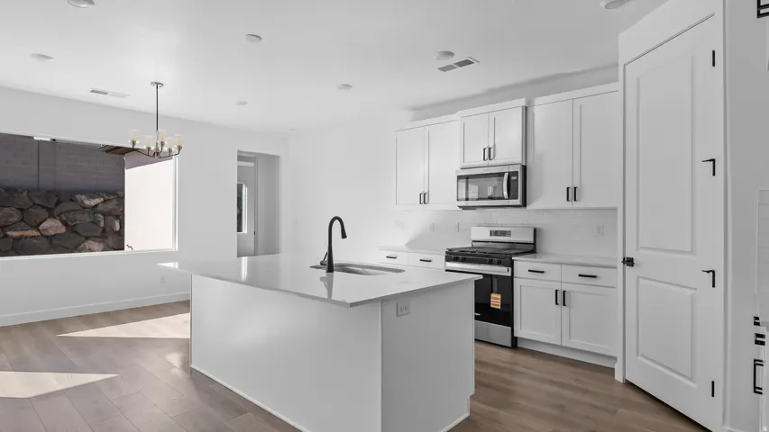 Kitchen with stainless steel appliances, white cabinetry, a kitchen island with sink, dark wood-style flooring, and light stone countertops