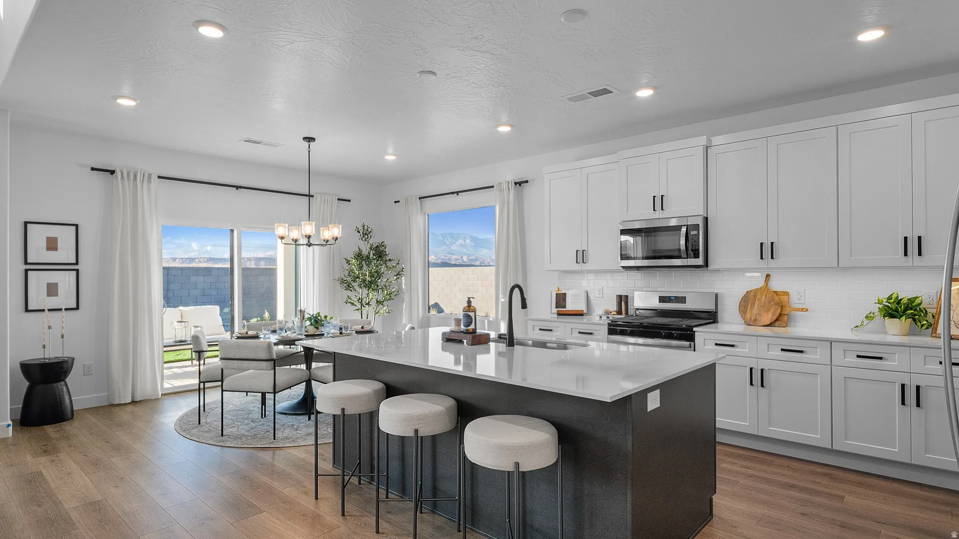 Kitchen featuring stainless steel appliances, light stone countertops, an island with sink, hanging lights, and dark wood-type flooring