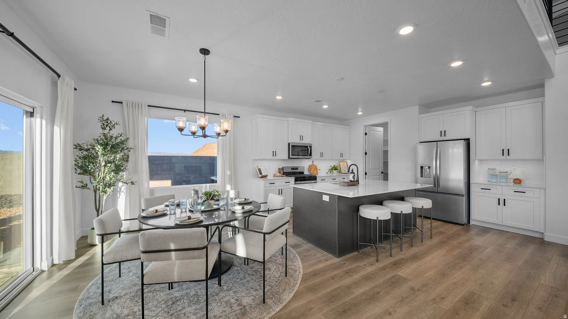 Kitchen with stainless steel appliances, an island with sink, a breakfast bar area, suspended lighting, and light stone counters