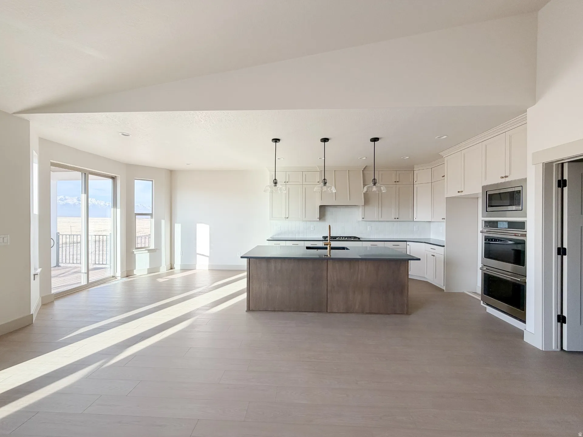 Kitchen with open floor plan, a kitchen island with sink, dark countertops, appliances with stainless steel finishes, and hanging light fixtures