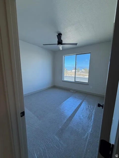 Carpeted spare room featuring a textured ceiling and ceiling fan