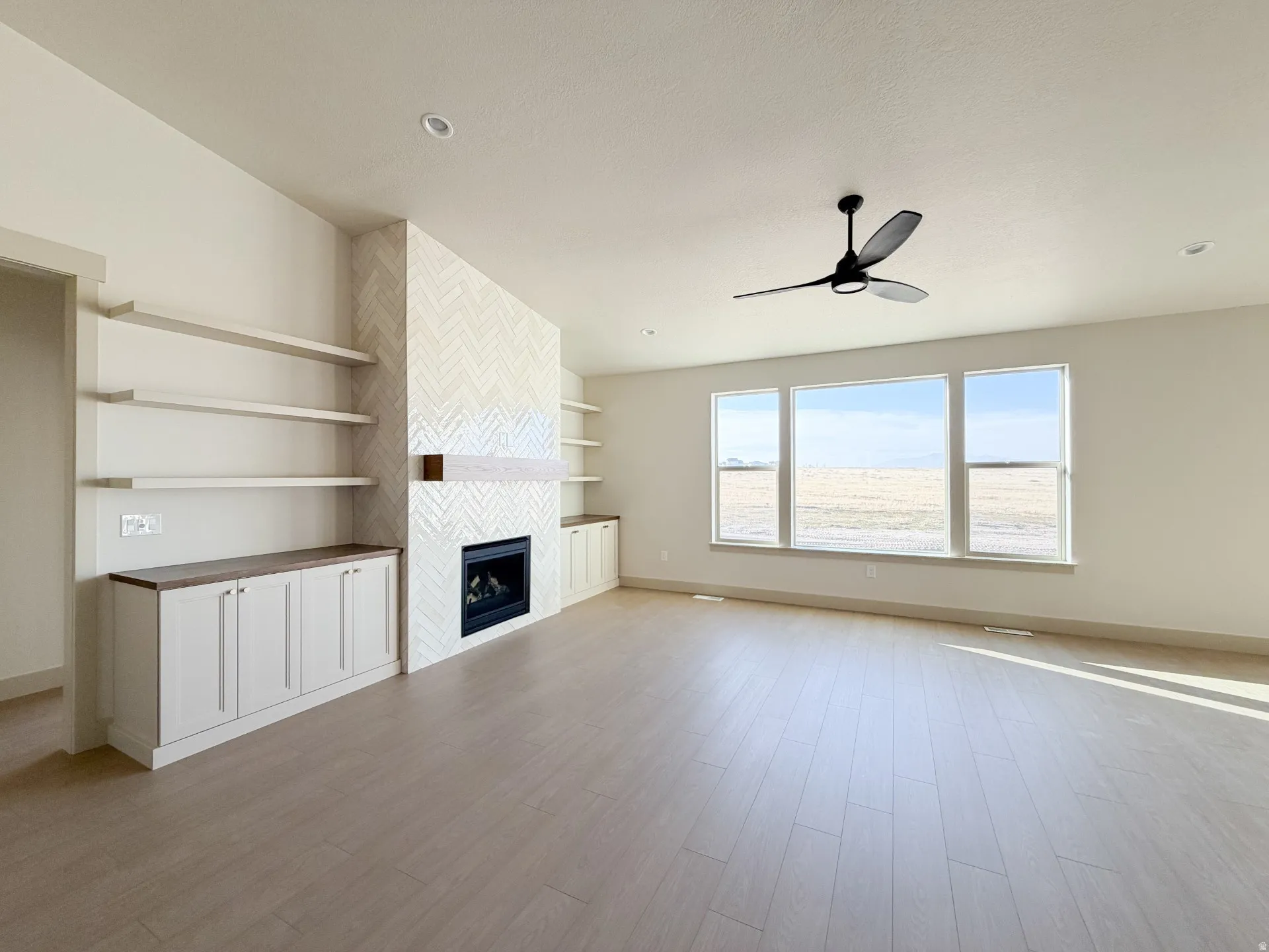 Unfurnished living room with a fireplace, light wood-type flooring, and a ceiling fan