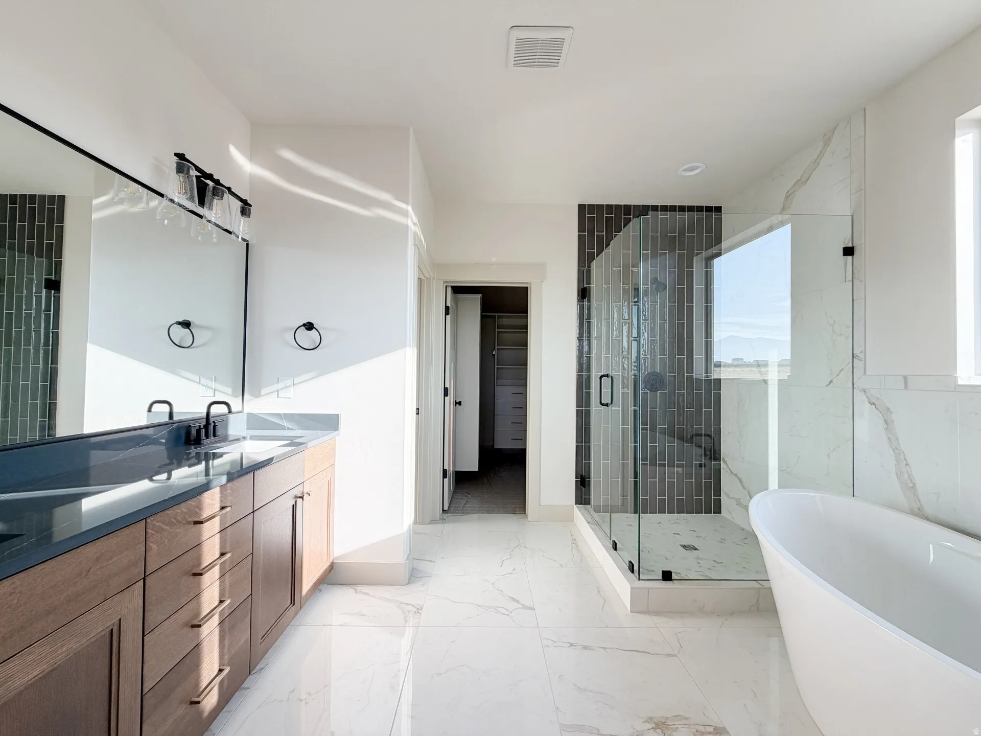 Bathroom with a shower stall, a soaking tub, a walk in closet, double vanity, and light marble finish floors