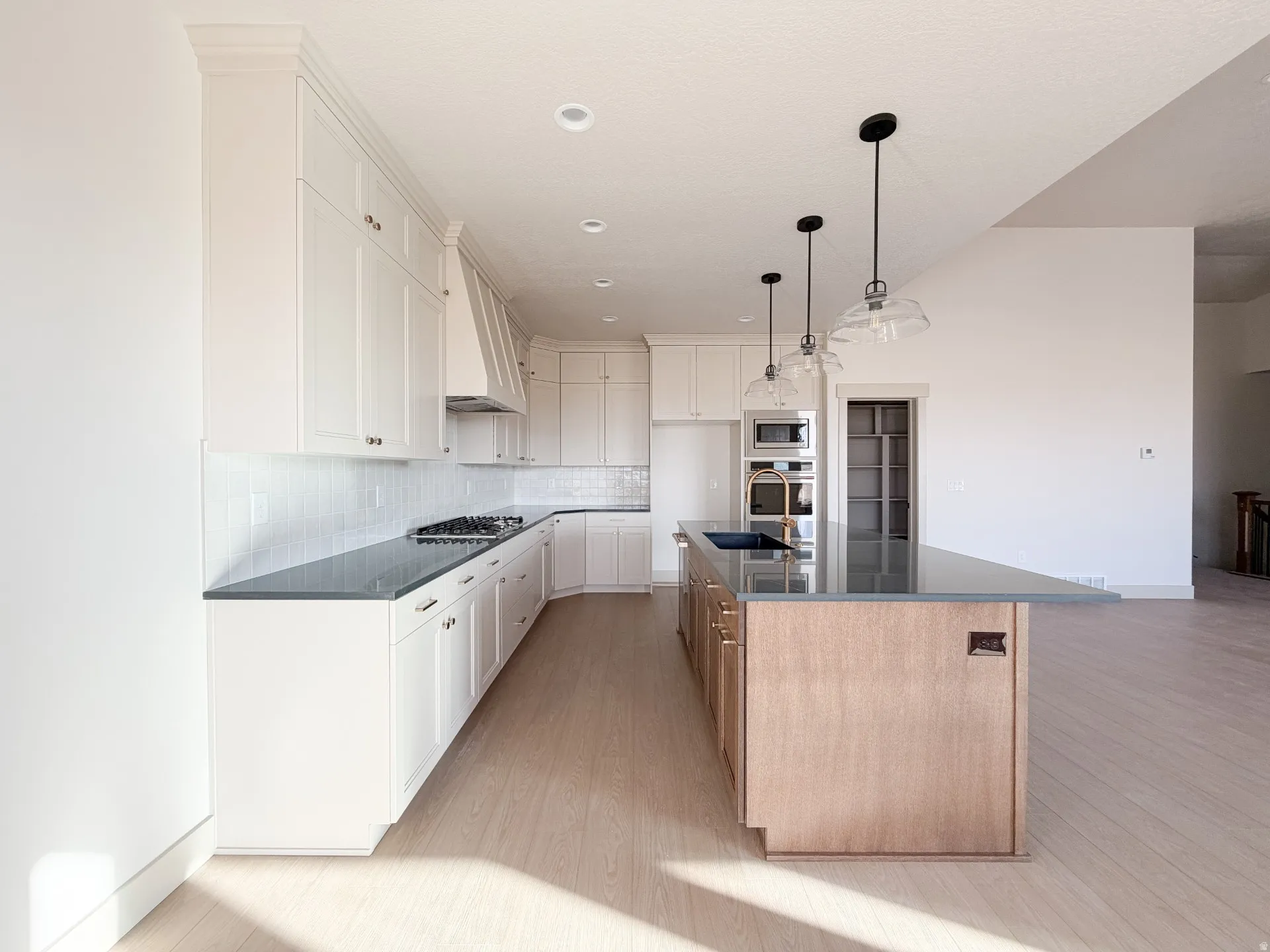Kitchen with backsplash, a center island with sink, light wood finished floors, white cabinets, and recessed lighting