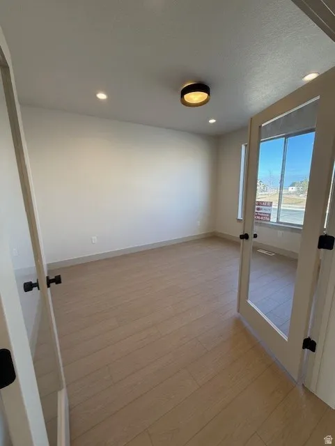 Empty room with light wood-style floors, recessed lighting, french doors, and a textured ceiling
