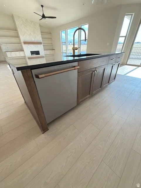 Kitchen with light wood-type flooring, stainless steel dishwasher, an island with sink, dark countertops, and recessed lighting