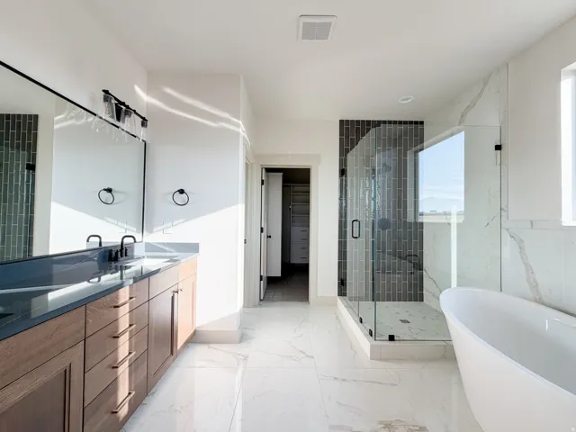 Bathroom with a shower stall, a soaking tub, a walk in closet, double vanity, and light marble finish floors