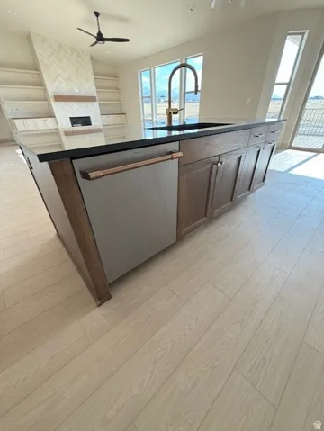 Kitchen with light wood-type flooring, stainless steel dishwasher, an island with sink, dark countertops, and recessed lighting