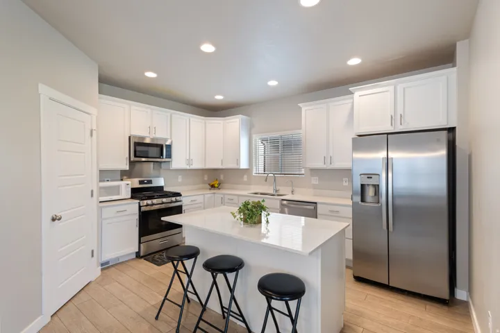 Kitchen featuring stainless steel appliances, white cabinets, a kitchen bar, light wood-style flooring, and light stone countertops