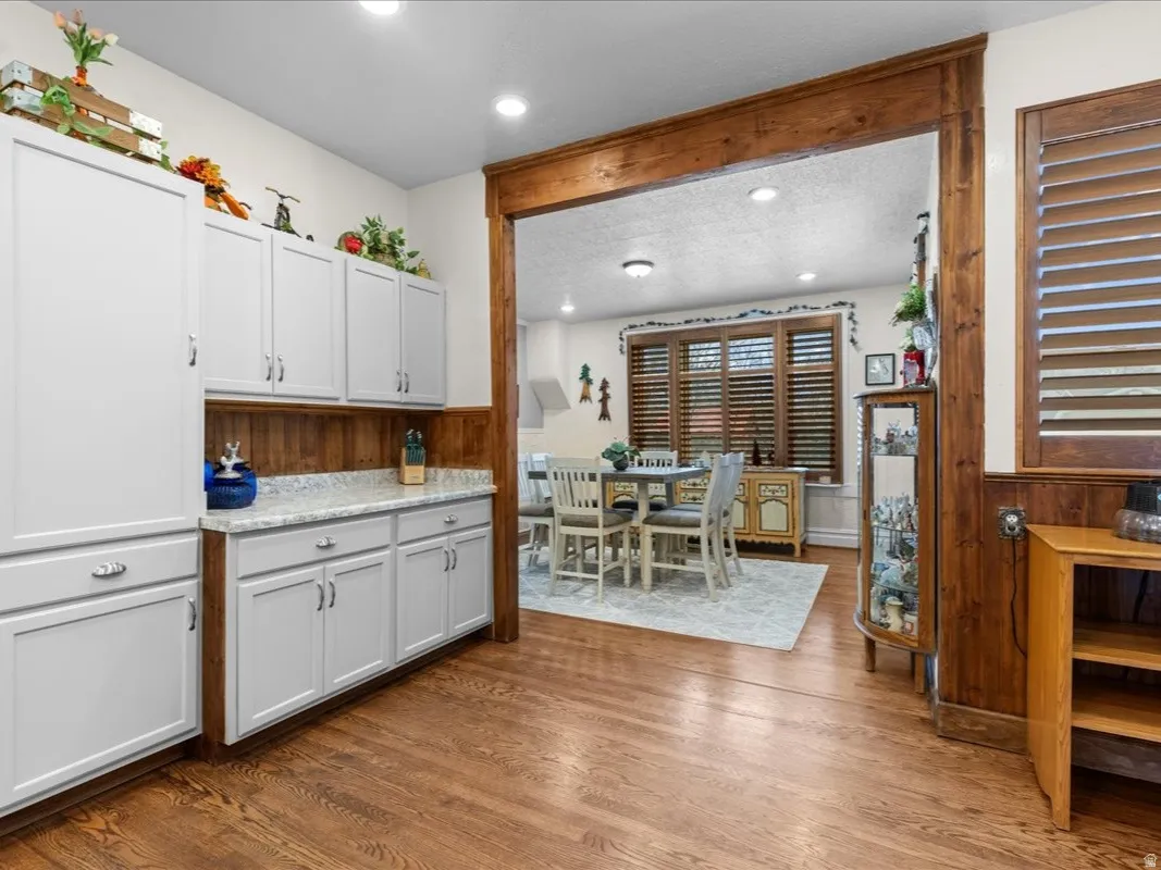Kitchen with dark wood-type flooring, recessed lighting, wainscoting, white cabinetry, and wooden walls