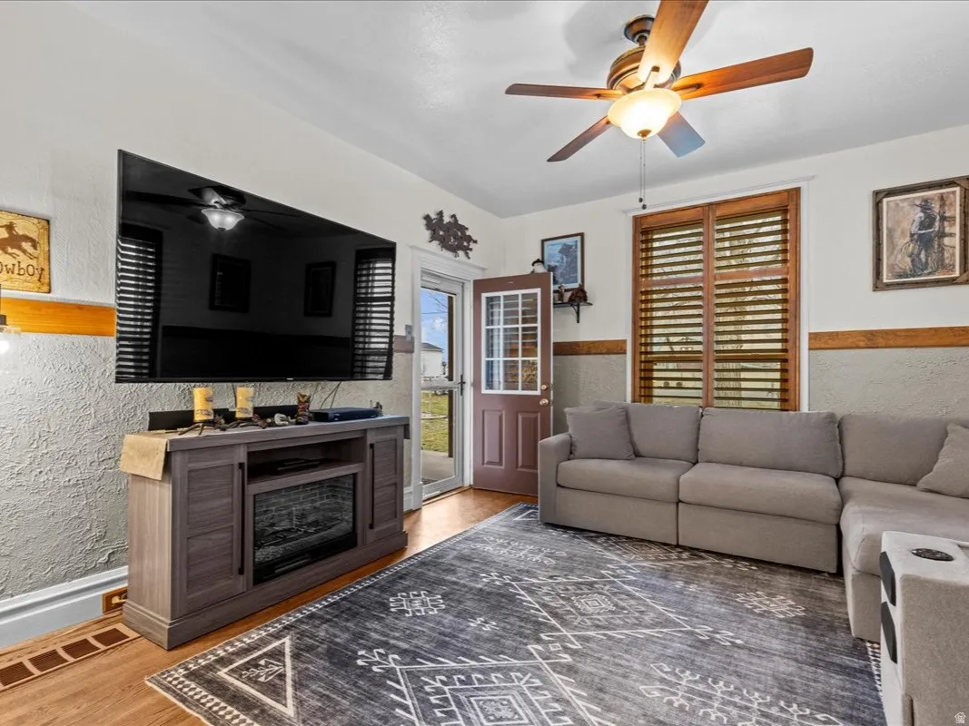 Living area with a ceiling fan, light wood-style floors, a textured wall, and wainscoting