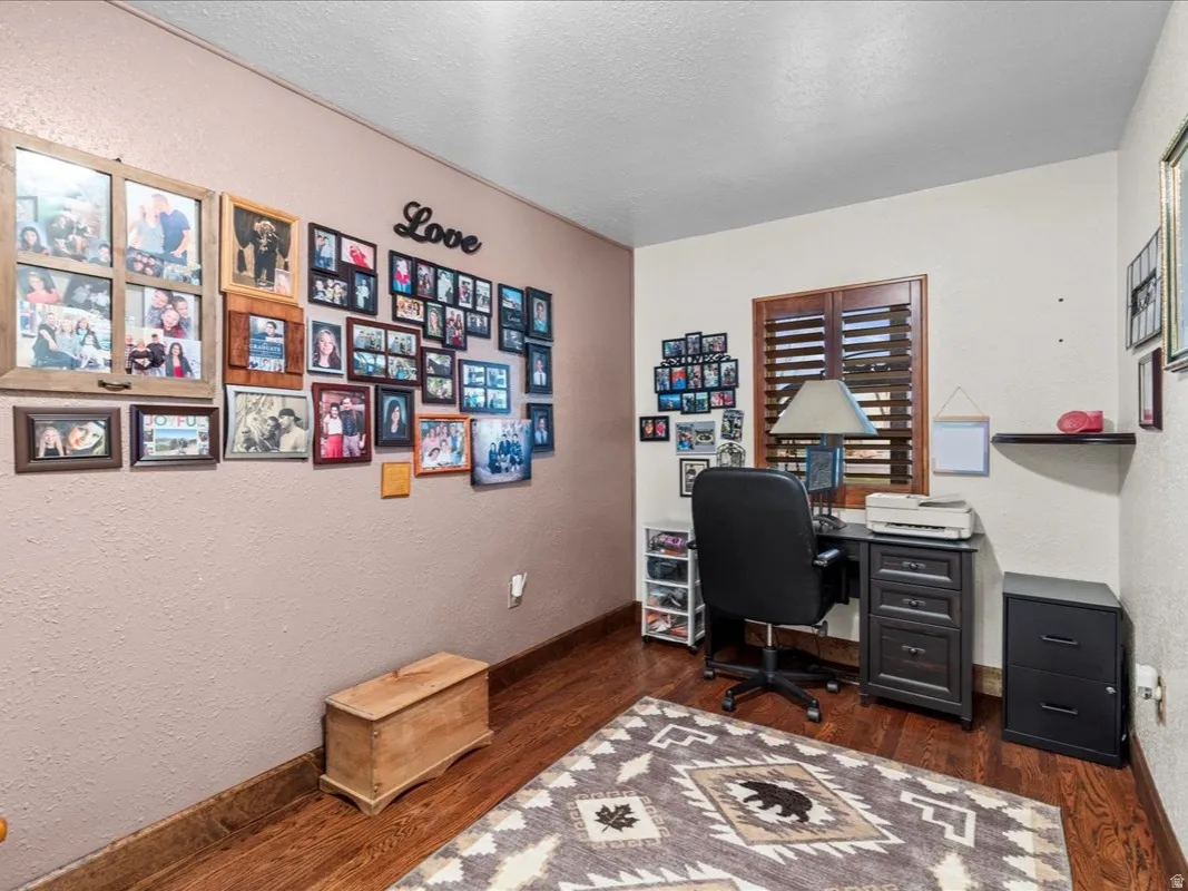 Office area with a textured wall, dark wood-style floors, and a textured ceiling