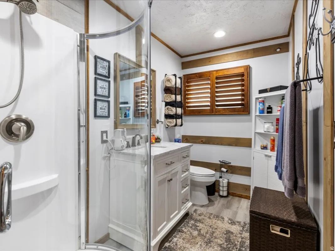 Full bath with vanity, a shower stall, ornamental molding, light wood finished floors, and a textured ceiling