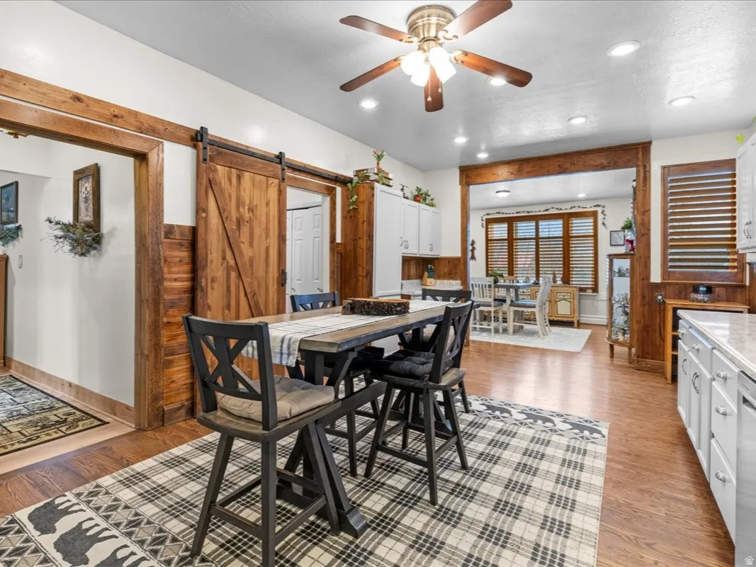 Dining space with a barn door, light wood-type flooring, a ceiling fan, and recessed lighting