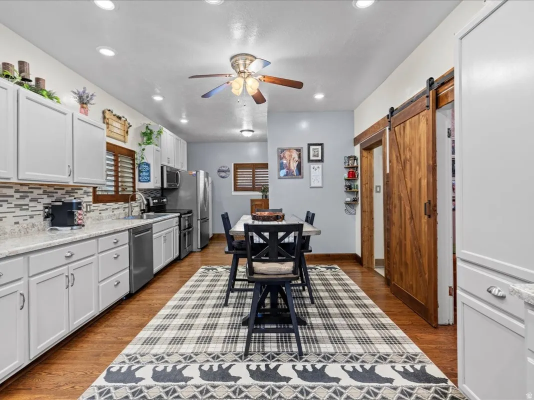 Kitchen with white cabinets, a barn door, appliances with stainless steel finishes, tasteful backsplash, and ceiling fan